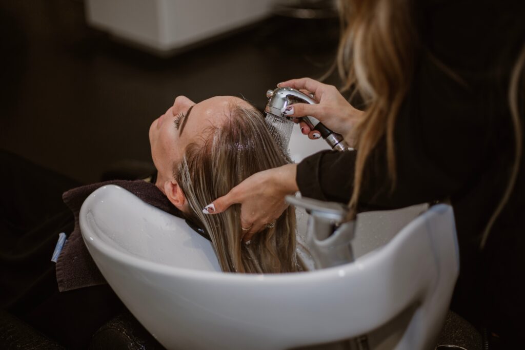 stylist washing clients hair in the shampoo bowl, picture taken at the side of the stylist on her left side 