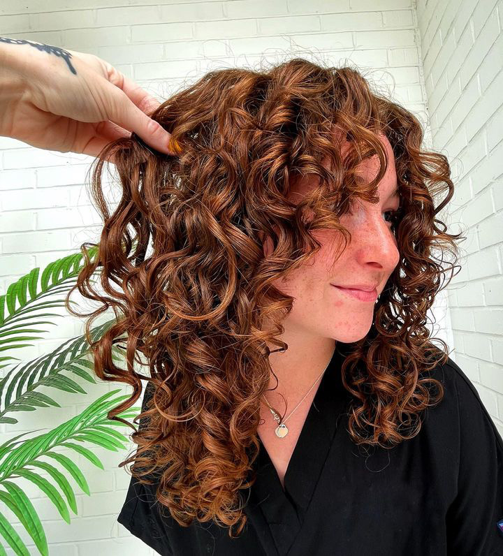 A girl with beautiful red-brown hair with natural curls styled to frame her face. Created  with curly hair products