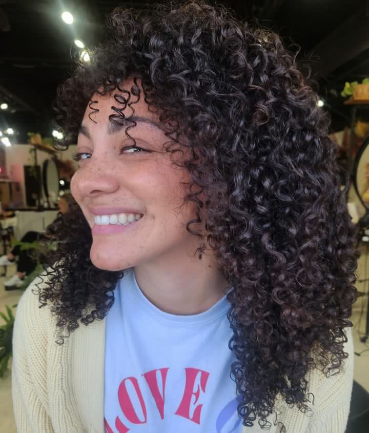 A curly girl with super dark hair and a few subtle bang pieces that frame her face perfectly. styled with curly hair products