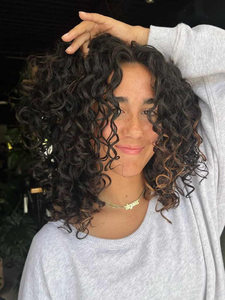 Super dark hair with pops of blonde on the ends cut into a just above the shoulder style with super curly hair. styled with curly hair products


